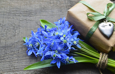 Bouquet of Blue Scilla (Squill) flowers and gift box with vintage silver heart on old wooden table.Happy Mother's Day or Spring holidays decoration.Spring flowers for Mother's Day.Selective focus.