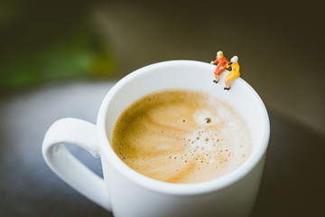 Miniature people couple ladies sitting on cup of coffee