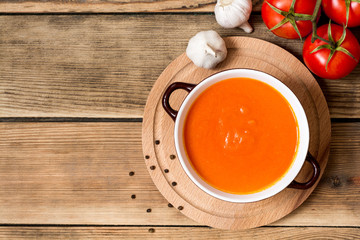 Tomato soup in ceramic bowl on wooden background.