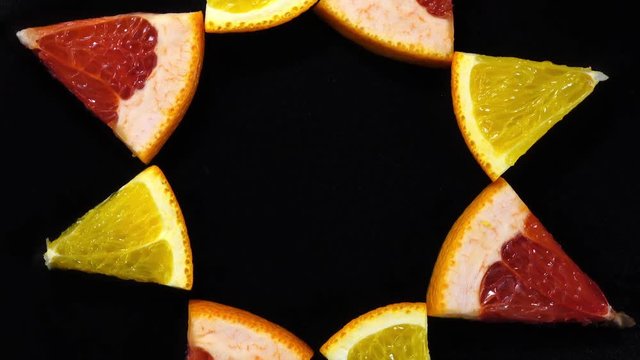 Excellent top view of orange and red grape-fruit sector slices, put in sun on black dish, rotating clockwise. Concentric flat lay of yummy pieces of dessert on dark background with amazing texture