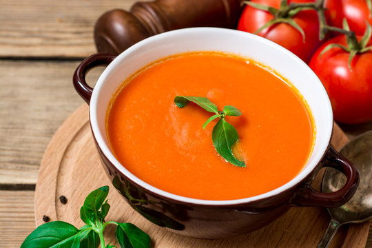 Tomato soup in ceramic bowl on wooden background.
