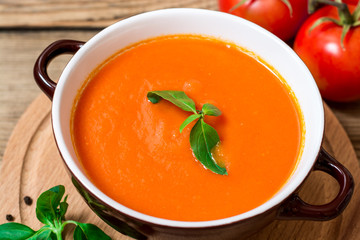 Tomato soup in ceramic bowl on wooden background.