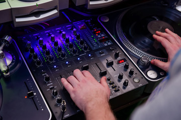 Close up Dj hands on equipment deck and mixer with vinyl record at party. Top view, selective focus