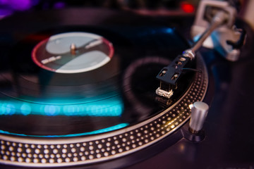 Turntable playing vinyl close up with needle on the record with coloured light background. Selective focus