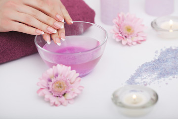Obraz na płótnie Canvas Spa Procedure. Woman In Beauty Salon Holding Fingers In Aroma Bath For Hands. Closeup Of Female Nails Soaking In Bowl Of Water With Pink Flower Petals. Aromatherapy. High Resolution