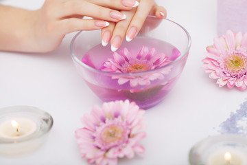 Obraz na płótnie Canvas Spa Manicure. Woman Hands With Perfect Natural Healthy Nails Soaking In Aroma Hand Bath. Closeup Of Glass Bowl With Water And Blue Sea Salt For Spa Procedure. Professional Nail Care. High Resolution