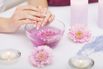 Fototapeta na wymiar Spa Procedure. Woman In Beauty Salon Holding Fingers In Aroma Bath For Hands. Closeup Of Female Nails Soaking In Bowl Of Water With Pink Flower Petals. Aromatherapy. High Resolution