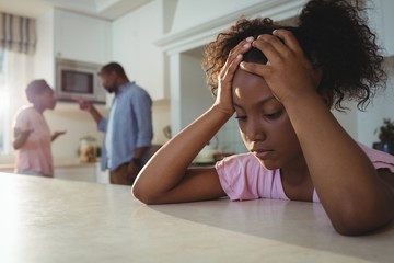 Sad girl listening to her parents arguing in kitchen