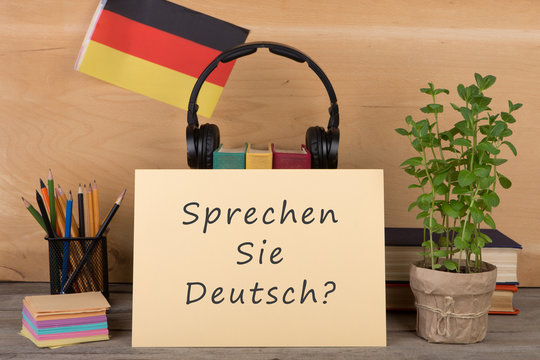 paper with text "sprechen sie deutsch?", flag of the Germany, books, headphones, pencils
