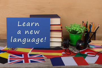 paper with text "Learn a new language!", flags, books, headphones, pencils