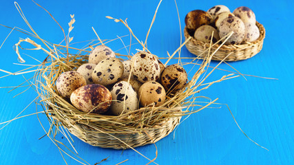 Fresh organic quail eggs in rustic wicker baskets on blue table. Horizontal, close up, selective focus, copy space. top view.