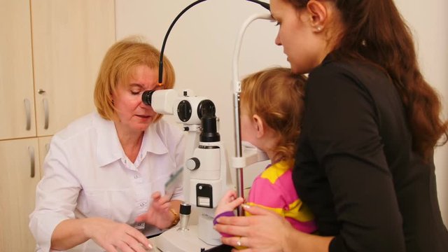 Woman optometrist checks eyesight at little girl - child's ophthalmology