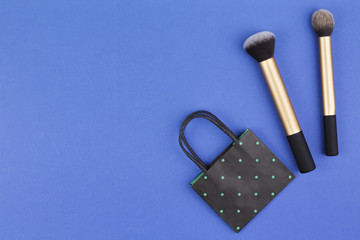Make up brushes with black polka dot paper shopping bag on blue background