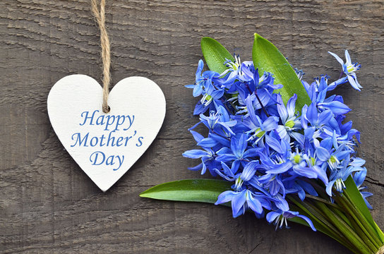 Happy Mother's Day.Blue Scilla flowers and decorative wooden heart on old wooden background.Mother's Day greeting card.Selective focus.