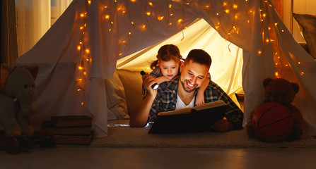 Obraz na płótnie Canvas happy family father and child reading book in tent at home.