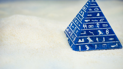 Abstract blue pyramid with hieroglyph staying on sand