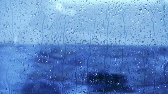 Close-up of water droplets on glass window with reflection.