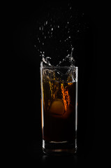 A glass of whiskey and ice cube on a black background