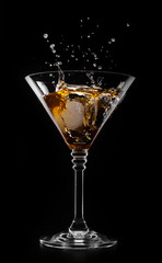 A glass with vermouth and ice cube on a black background
