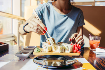 Woman in the blue shirt is eating at a sushi restaurant in summer