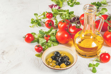 Ingredients of Italian cuisine. Selection of products for salad. Olive oil, lettuce leaves, tomatoes. On a white concrete stone kitchen table. copy space