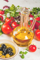 Ingredients of Italian cuisine. Selection of products for salad. Olive oil, lettuce leaves, tomatoes. On a white concrete stone kitchen table. copy space