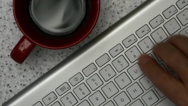 Elderly Man Is Typing On A Keyboard. On The Table Is A Cup Of Coffee