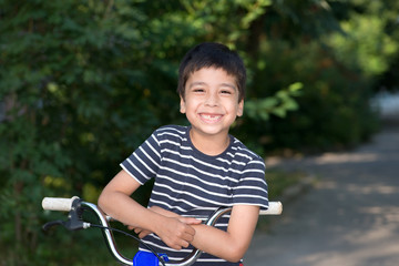 Obraz premium the boy with bicycle stands on the street and smiles