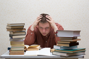 Confused guy sitting at a table with a pile of books