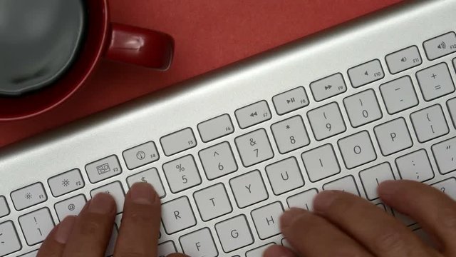 Elderly Man Is Typing On A Keyboard. On The Table Is A Cup Of Coffee. Red Background.