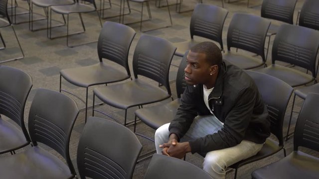 Single, alone, male sitting in crowd of chairs looking up at stage in hope.
