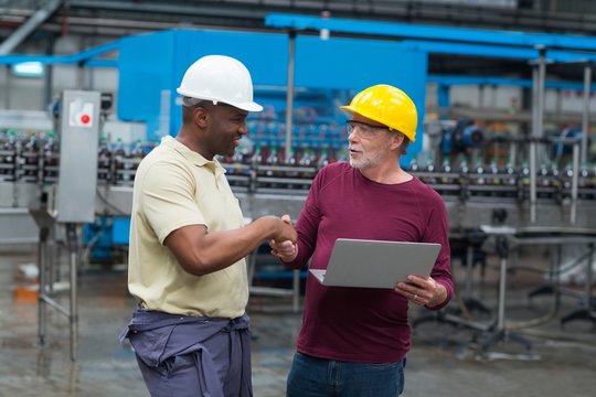 Factory workers with laptop shaking hands with his colleague