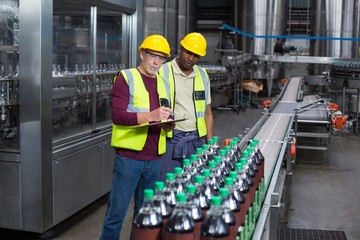 Two factory workers monitoring cold drink bottles in the plant