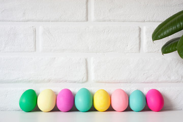 Easter colored eggs against white brick wall, scandinavian nordic flower on table. Cute Easter celebration decoration background. Copy space for text. Happy Easter vacation concept. Easter card.