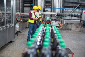 Two factory workers monitoring cold drink bottles 