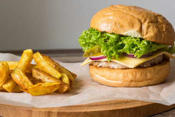 Home made hamburger with chicken, onion, cucumber, lettuce and cheese on wooden table with potato fries