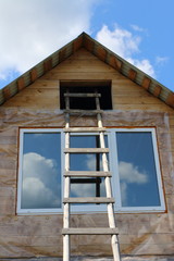Ladder to the attic of a village log house under construction against a blue sky