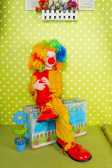 Obraz na płótnie Canvas A cheerful clown in an iridescent wig and huge boots stands on a luscious bright green background in polka dots