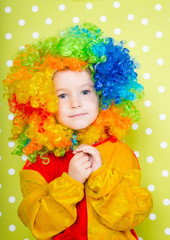 A cheerful clown in an iridescent wig and huge boots stands on a luscious bright green background in polka dots