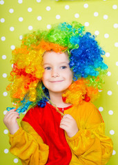 A cheerful clown in an iridescent wig and huge boots stands on a luscious bright green background in polka dots