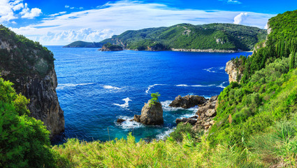 Beautiful summer panoramic seascape. View of the coastline into the sea bays with crystal clear azure water. Lonely rock with a tree on top. A small tree on top. Paleokastrica. Corfu. Greece.