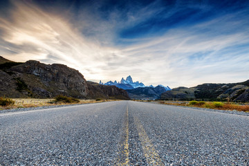 The road approaching the town of El Chalten with famous Patagonia mountains, including Cerro Fitz Roy, in the background at golden hour