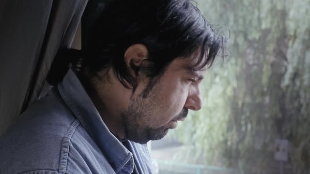 A sick man badly coughing, standing near a window on a cold day.
