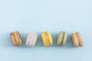 Row of colorful french macaroons on blue background. Top view, copy space for text. Social media, blogging concept 