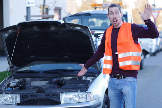 Mann in Warnweste bei seinem liegengebliebenen Auto  