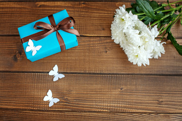 Wooden background with a gift and flowers and butterflies. Top view.  The concept of Mother's Day, birthday, March 8.