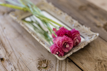 Fototapeta na wymiar Small bouquet of pink ranunculus flower lying on vintage tray
