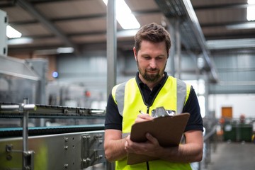 Factory worker writing on clipboard in factory