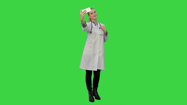 Young pretty female doctor makes selfie on smart phone smiling on a Green Screen, Chroma Key.