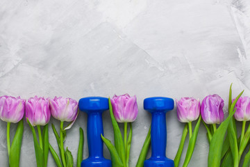 Spring flatlay sport composition with blue dumbbells and purple tulips.